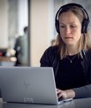 Kvinde sidder foran computer med høretelefoner og ser dybt koncentreret ud.