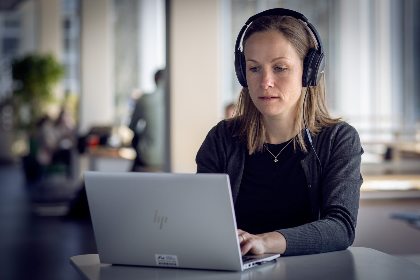 Kvinde sidder foran computer med høretelefoner og ser dybt koncentreret ud.