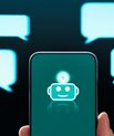 En hånd holder en telefon med et billede af et chatbot-ikon på skærmen. Ud fra skærmen går 4 talebobler.