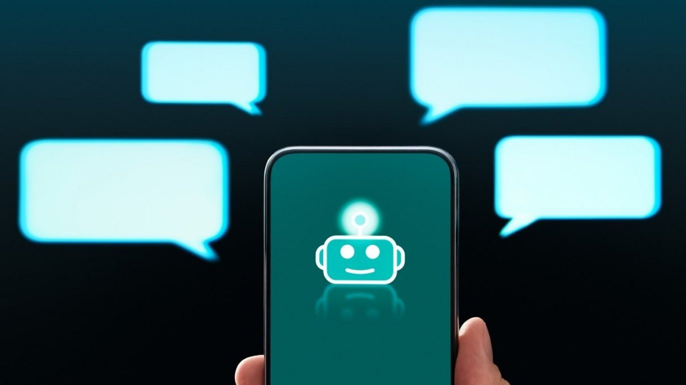 En hånd holder en telefon med et billede af et chatbot-ikon på skærmen. Ud fra skærmen går 4 talebobler.