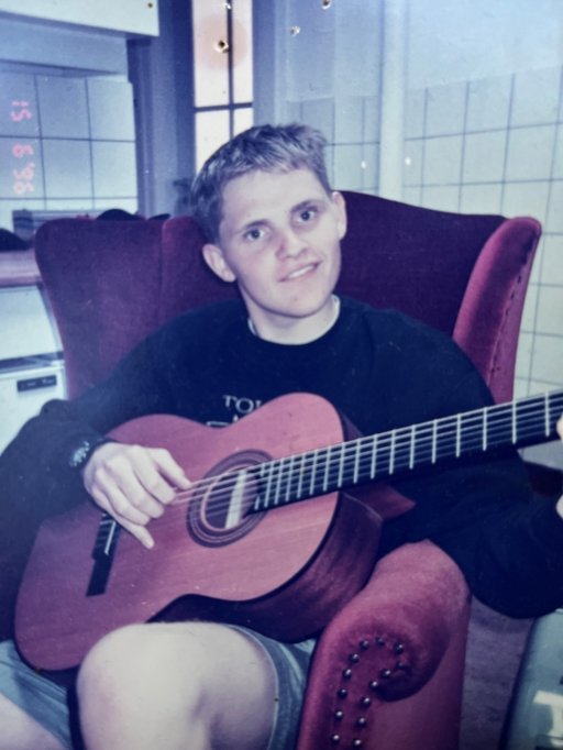 Asser Thomsen som ung studerende, siddende med en guitar. Billedet er fra cirka 1997.